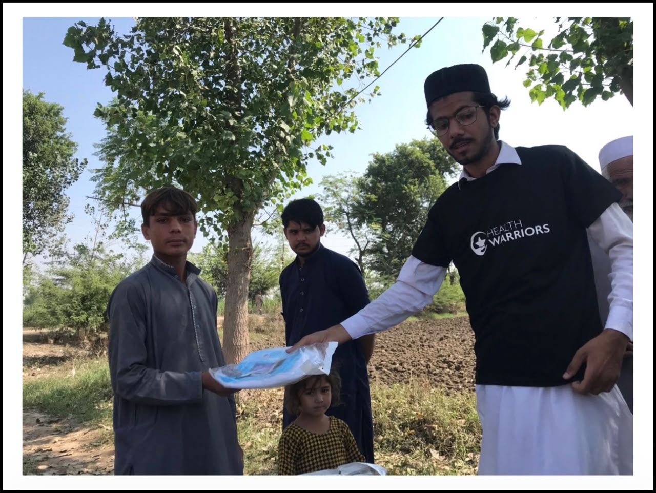 Health Warriors volunteer handing a wrapped mosquito net to a child outdoors